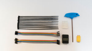 An assortment of electronic components, including two rainbow-colored ribbon cables with female headers, a stack of black zip ties, a small digital display showing "8.8.8", a small heatsink/thermal pad, and a blue hex wrench. These items appear on a white surface and are essential for Vikas integrations